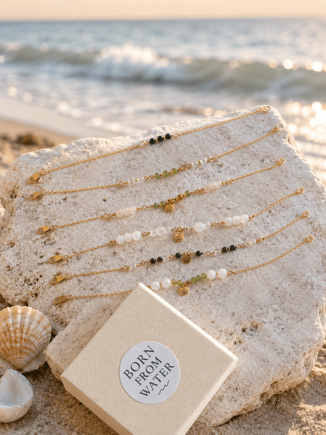 Born From Water gemstone bracelets arranged on coral rock beside the ocean